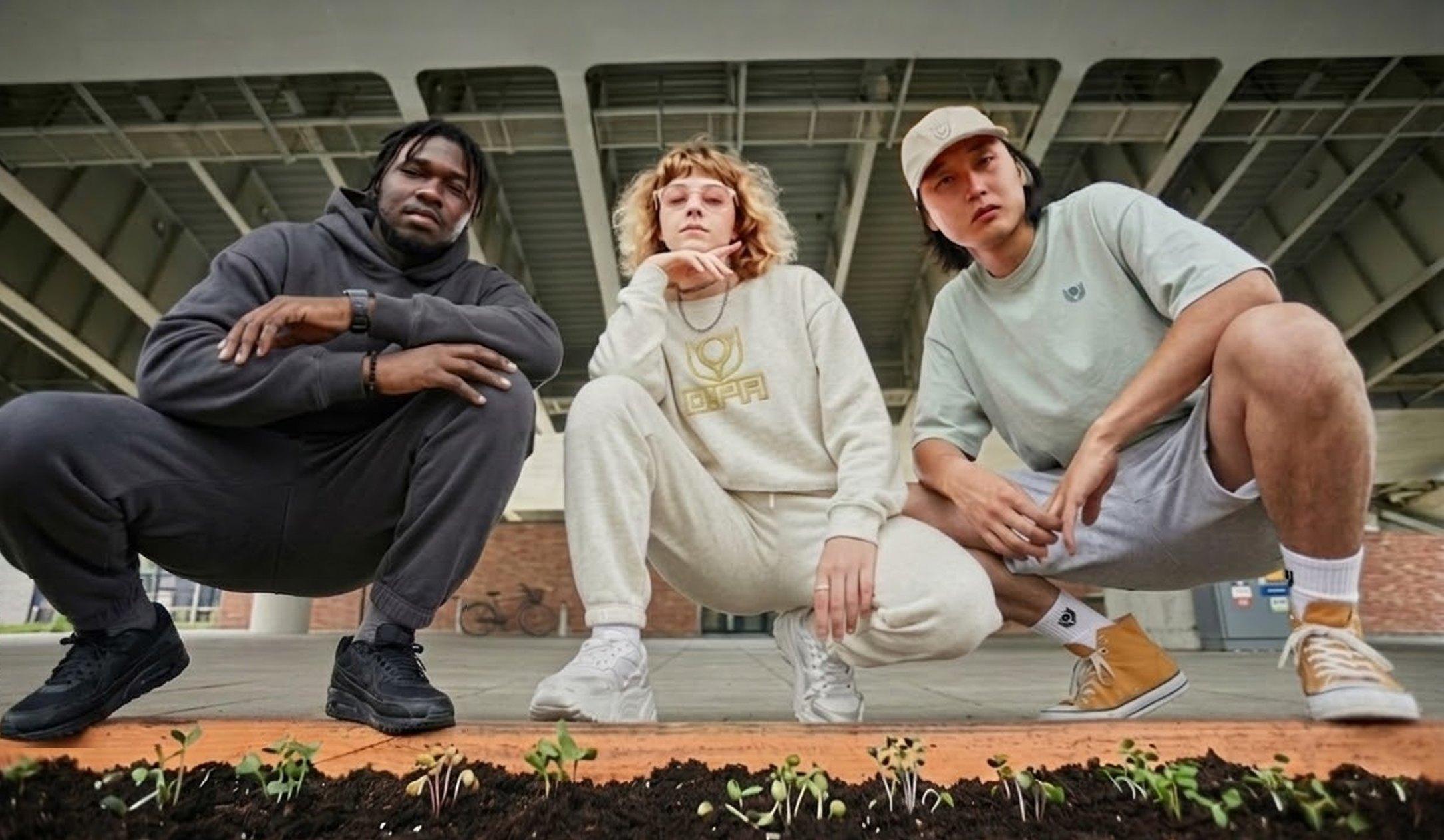 Three people in O!PA clothing crouching behind a bed of seedlings